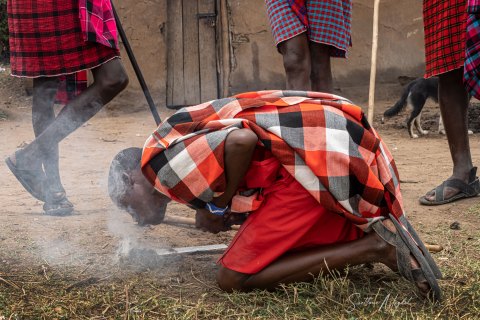 SVM_7847 
Maasai Man in traditional  colourful   warrior outfit; red shuka cloth starting fire catching sun with blade